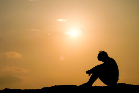 A solitary figure sits in contemplation against a stunning sunset, creating a peaceful and reflective scene.の写真素材