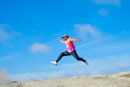 A dynamic shot of a fit athlete in mid-air, leaping with enthusiasm against a vibrant blue sky backdrop.の写真素材