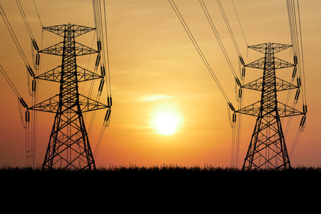 Silhouetted power lines and transmission towers against a vibrant orange sunset sky, capturing the essence of energy and infrastructure.の写真素材