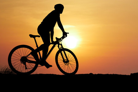 A silhouette of a cyclist on a mountain bike against a stunning sunset backdrop with an orange sky.の写真素材