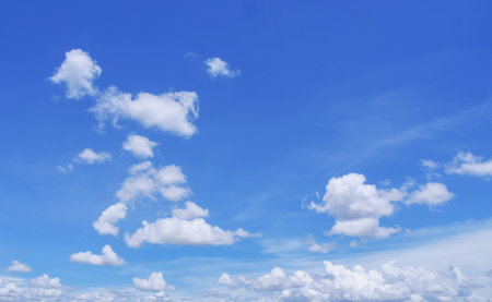 A serene image of a clear blue sky with scattered white fluffy clouds, perfect for backgrounds, nature themes, and peaceful settings.の写真素材