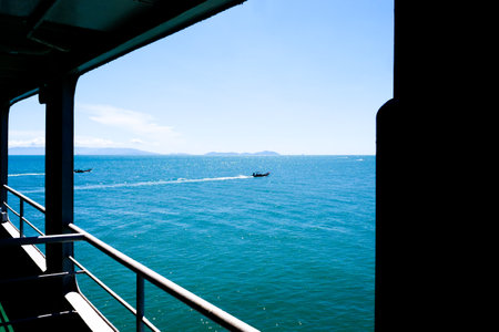 A serene view of the ocean from a boat deck, featuring clear blue skies, calm waters, and distant...