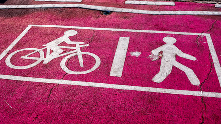 Close-up of white bicycle and pedestrian symbols on a bright pink asphalt pathway, showing wear and cracks.の写真素材