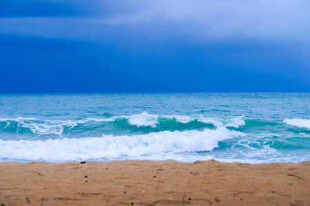 A tranquil beach scene featuring gentle waves crashing onto the sandy shore under a dramatic, cloudy sky.の写真素材