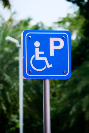 Close-up of a blue handicap parking sign with a white symbol, set against a backdrop of green foliage and trees.の写真素材
