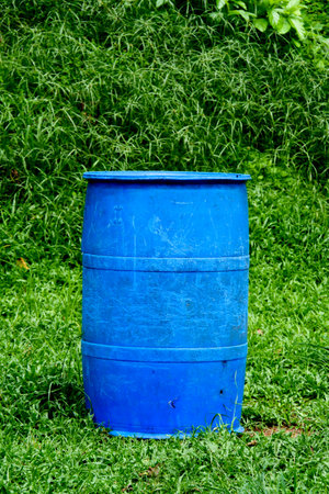 A vibrant blue plastic barrel standing on a green grass field, surrounded by lush foliage in an outdoor environment.の写真素材