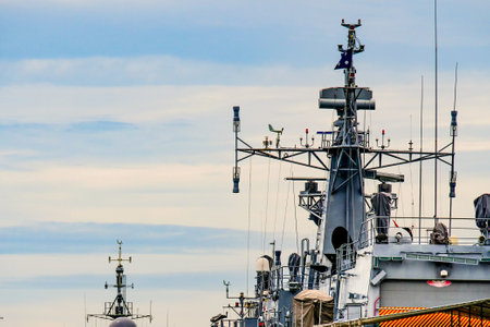 Close-up of a naval warship's communication towers and radar systems under a cloudy sky, showcasing modern maritime technology.の写真素材