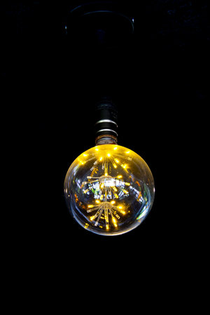 Close-up of a glowing vintage Edison bulb with visible filaments, set against a dark background,...