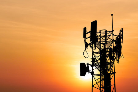 A communication tower silhouetted against a vivid orange sunset, showcasing antennas and cables in a serene evening setting.の写真素材