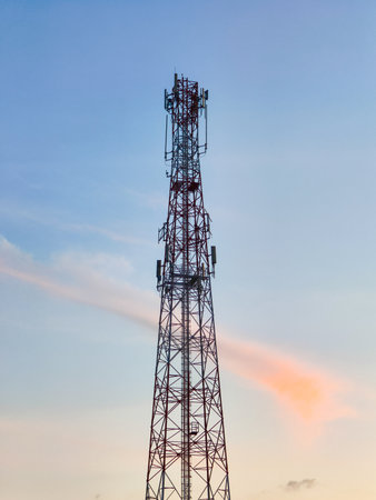 A tall telecommunication tower silhouetted against a colorful sunset sky, featuring soft pastel clouds and a serene atmosphere.の写真素材