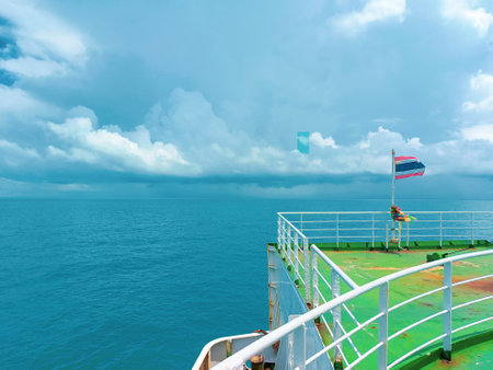 Peaceful ocean scene from a ship deck, featuring a national flag and vast blue sky with clouds.の写真素材