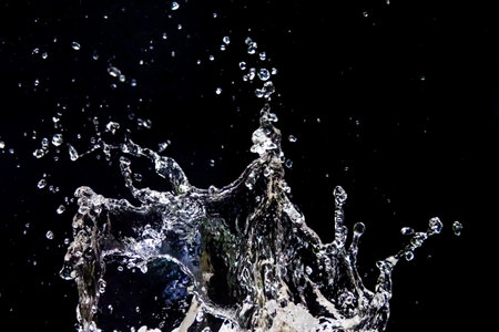 High-speed capture of water droplets splashing against a dark background, showcasing motion and energy.の写真素材