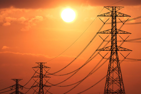 Power lines silhouetted against a vivid orange sunset sky, capturing the beauty of industrial structures in nature.の写真素材