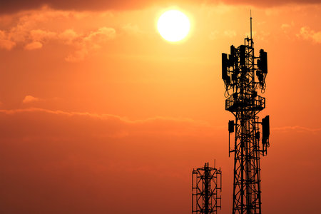 Communication towers silhouetted against a vivid orange sunset, highlighting the beauty of...