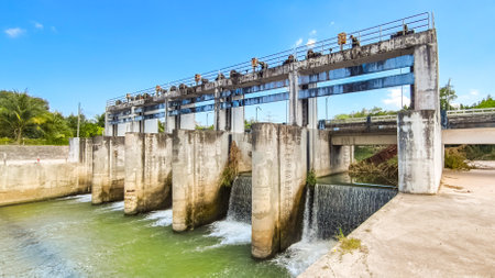 A concrete water dam with flowing water, surrounded by greenery and a clear blue sky, showcasing industrial architecture in a natural environment.の写真素材