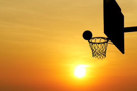 Silhouette of a basketball hoop set against a colorful sunset, capturing the essence of outdoor sports and evening tranquility.の写真素材