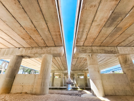 View from beneath a concrete bridge showcasing architectural lines, blue sky, and water reflections.の写真素材