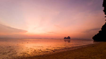 A breathtaking sunset over a serene beach, showcasing vibrant colors and silhouetted rock formations reflected on the calm water.の写真素材