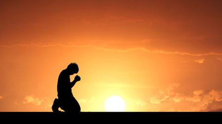 A silhouette of a person kneeling in prayer during a stunning sunset, creating a serene and contemplative atmosphere.の写真素材