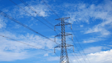 Tall electricity transmission tower with power lines stretching across a vibrant blue sky and scattered clouds.の写真素材