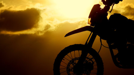 A striking silhouette of a motorcycle set against a dramatic sunset, highlighting the vibrant colors and golden clouds in the sky.の写真素材