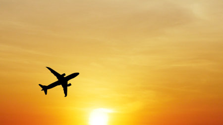 ** Airplane silhouette soaring through a vivid orange sunset sky, capturing the essence of travel and adventure.

**の写真素材