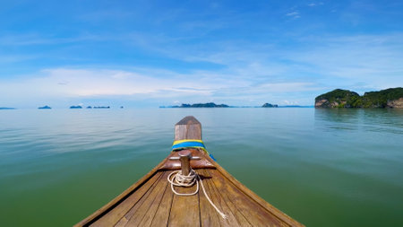 Serene scene from a longtail boat on calm waters, showcasing distant islands and a vibrant blue sky.の写真素材