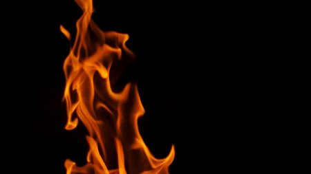 Close-up of vivid orange flames against a black background, showcasing the dynamic movement and energy of fire.の写真素材