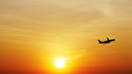 Silhouette of an airplane flying against a vivid orange sunset sky with the sun setting on the horizon.の写真素材