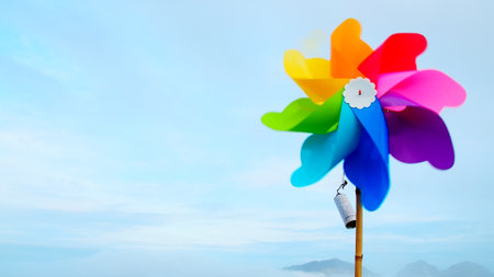 Vibrant multicolored pinwheel spinning against a clear blue sky with distant mountains, symbolizing joy and freedom.の写真素材