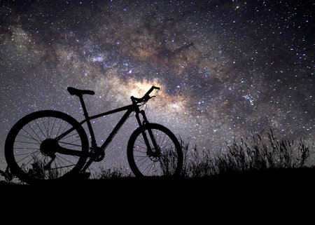 A mountain bike silhouette set against a stunning starry night sky, showcasing the Milky Way's...