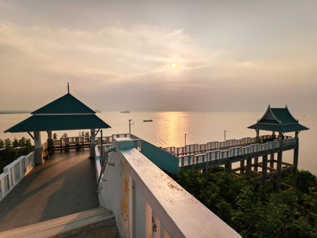 Elevated walkway with gazebos offers a breathtaking sunset view over a tranquil ocean, surrounded by lush greenery.の写真素材
