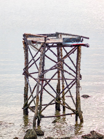 ** A rustic wooden fishing platform on stilts stands in calm coastal waters, showcasing traditional fishing methods and serene maritime scenery.

**の写真素材