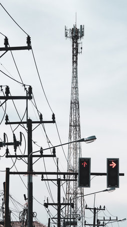 A cityscape featuring a communication tower, power lines, and traffic lights under a cloudy sky.の写真素材