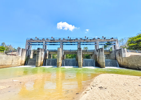 A modern dam with cascading water under a bright blue sky, surrounded by nature.の写真素材
