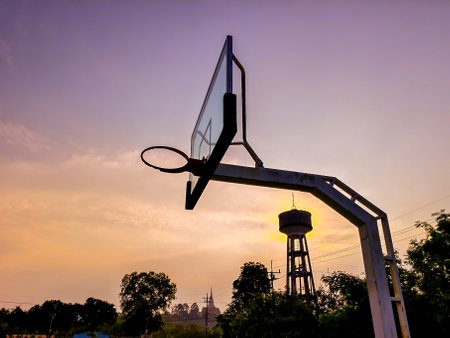 Silhouette of a basketball hoop at sunset with a water tower and trees in the background, capturing a serene evening scene.の写真素材