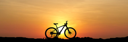 A bicycle silhouette set against a stunning sunset, showcasing vibrant orange and yellow hues in the...