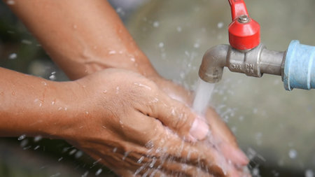 Close-up of hands being washed under a running outdoor faucet, emphasizing hygiene and cleanliness.の写真素材