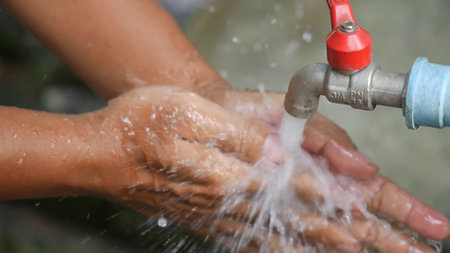 Hands being washed under a flowing outdoor faucet, emphasizing hygiene, cleanliness, and water conservation.の写真素材