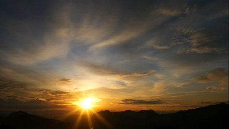 Captivating sunset scene with vibrant colors and dramatic clouds over a serene mountain landscape.の写真素材