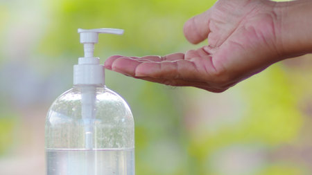 Hand applying sanitizer from a pump bottle outdoors, emphasizing hygiene and cleanliness in a natural setting.の写真素材