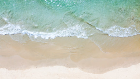 Aerial shot of a tranquil beach with turquoise waves gently lapping against the sandy shore,...