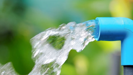 Clear water streaming from a blue PVC pipe with a lush green backdrop, symbolizing freshness and sustainability.の写真素材