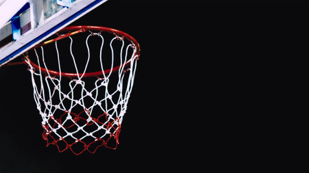 A detailed view of a basketball hoop with a red and white net against a dark backdrop, highlighting...