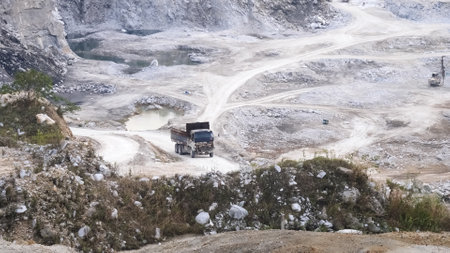 Aerial shot of a quarry featuring a dump truck navigating a winding dirt road amidst rocky terrain...