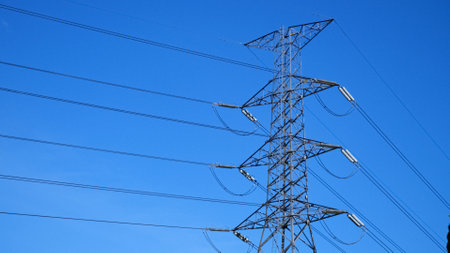 Steel transmission tower with power lines stretching across a bright blue sky, symbolizing energy...