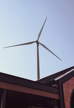 Wind turbine towering over a building, symbolizing renewable energy and sustainability against a...