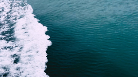 Stunning aerial shot capturing ocean waves meeting the shore, showcasing the contrast between white foam and deep blue sea.の写真素材