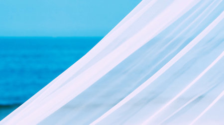 White fabric waves gently with the ocean breeze, set against a tranquil blue sea, creating a...