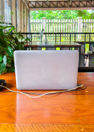 Open laptop on a wooden table in a bright outdoor setting, surrounded by lush greenery and natural light.の写真素材